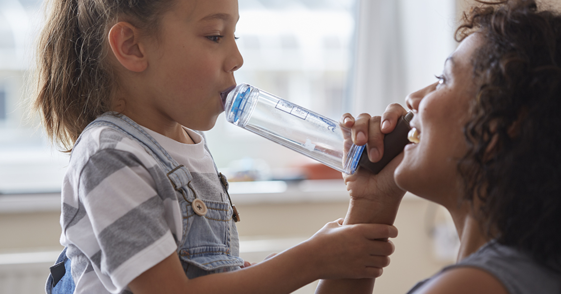 Smiling parent helping their child use an inhaler with a spacer 