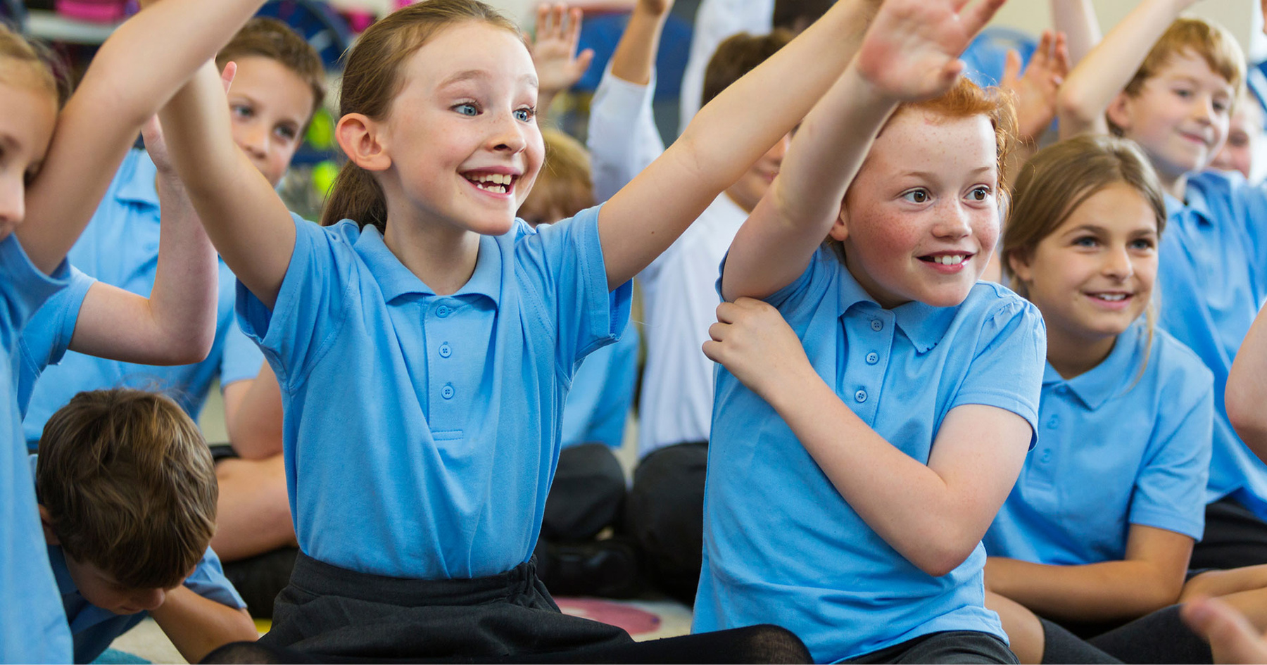 Excited pupils in school uniform with hands up