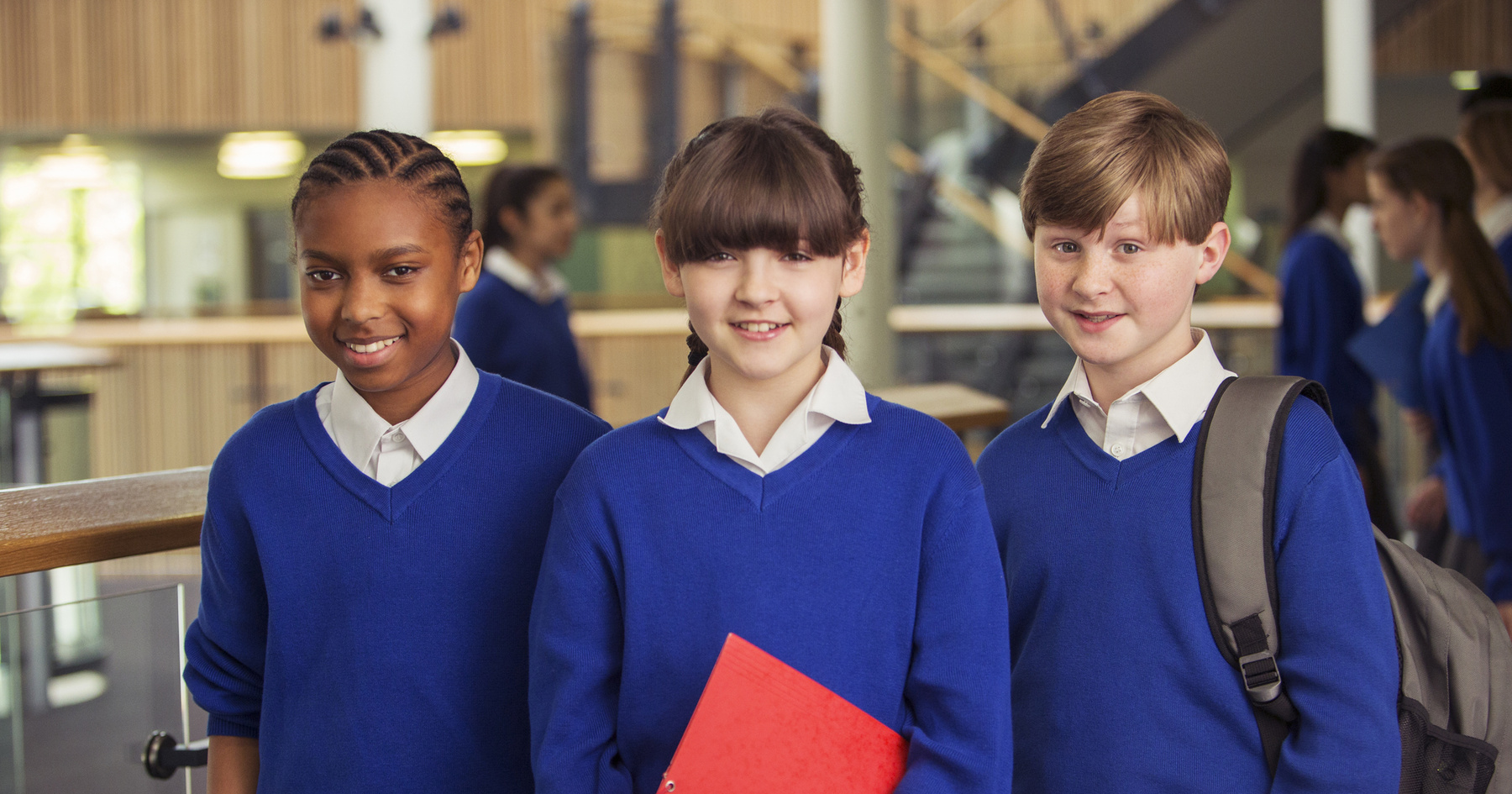 Image shows three school aged children in uniform, one is holding a red folder