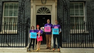A group of campaigners, including a child and a baby, stand outside 10 Downing Street holding boxes with messages about the impact of toxic air