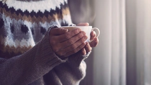 A person wearing a jumper and holding a mug with a hot drink