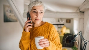 A woman in a yellow jumper holding a mug and speaking on the phone