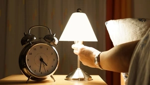 A clock and a lit up lamp on a bedside table