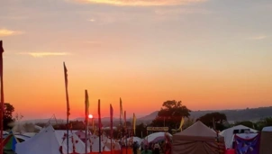 A festival campsite at sunset, with colourful flags lining a pathway between tents