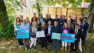 A group of people gathered outdoors holding signs advocating for clean air, with messages supporting the Clean Air Justice Network and Asthma + Lung UK