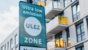 A sign marking an Ultra Low Emission Zone (ULEZ) stands in front of modern apartment buildings with glass balconies