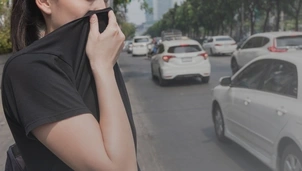 A person in a black shirt covers their nose and mouth with their clothing while standing next to a busy road filled with cars