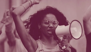 A woman with raised fists and a megaphone passionately speaks at a protest, surrounded by other demonstrators