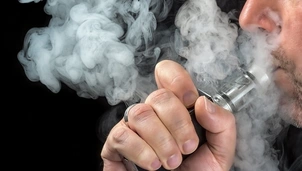 A close-up of a person using a vape device, exhaling thick clouds of vapour against a dark background