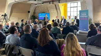 A room full of people listens to a panel discussion on "The Future of London Transport," with a banner and screen displaying the event’s theme