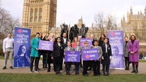 A group of adults and children hold signs supporting lung health outside the UK Parliament, with banners and historic buildings in the background
