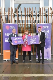 holding signs supporting lung health, with banners for Asthma + Lung UK Scotland in the background