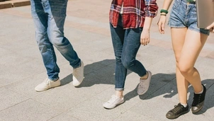 Three people walk together, showing only their legs in casual jeans, shorts, and trainers