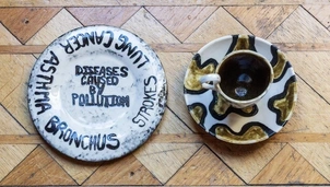 Two ceramic plates and a cup with an artistic design highlighting the impact of pollution, with one plate listing diseases like asthma, lung cancer, and strokes