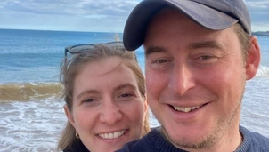 Smiling couple taking a selfie on a beach with the ocean in the background