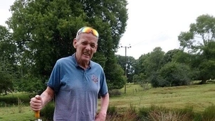 Man enjoying a walk outdoors, holding an umbrella, with a lush green landscape in the background