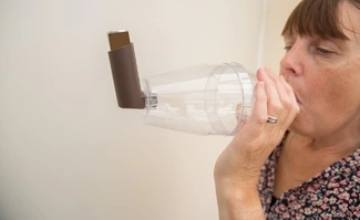 A woman using an inhaler with a transparent spacer