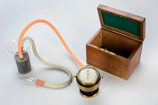 A vintage spirometer with tubes and a wooden storage box, used for measuring lung capacity