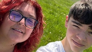 A woman with red hair and glasses and a young boy smiling in a sunny green field