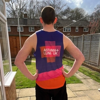 A man standing in a garden with his back to the camera, wearing an Asthma + Lung UK running vest