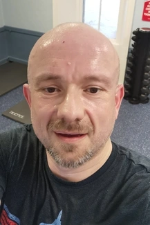 Man sweating and smiling in a gym setting with weights and exercise mats in the background