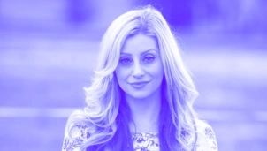 Woman with long, wavy blonde hair, smiling slightly, with a soft-focus background