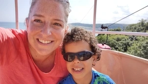 A woman and a child smiling on a cable car ride with a scenic view in the background