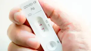 A hand holding a COVID-19 test displaying a positive result, indicated by the presence of two coloured lines