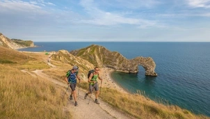 Two trekkers walking along the coast. Durdle Door is in the background.