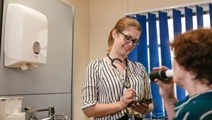 Person doing a peak flow test in front of a nurse